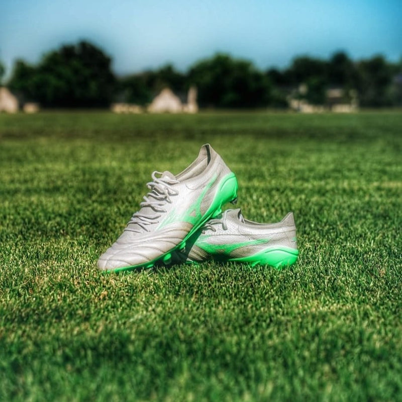 Silver and green Mizuno rugby boots on a sunlit grass pitch