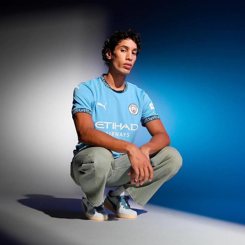 A model crouching in the light blue Puma Manchester City home shirt